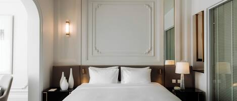 A hotel room with a large bed, two bedside tables, a chair, and a large window with blinds.