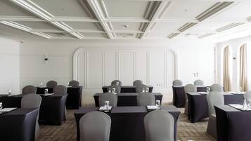 A conference room with tables and chairs, white walls, and a ceiling with recessed lighting.