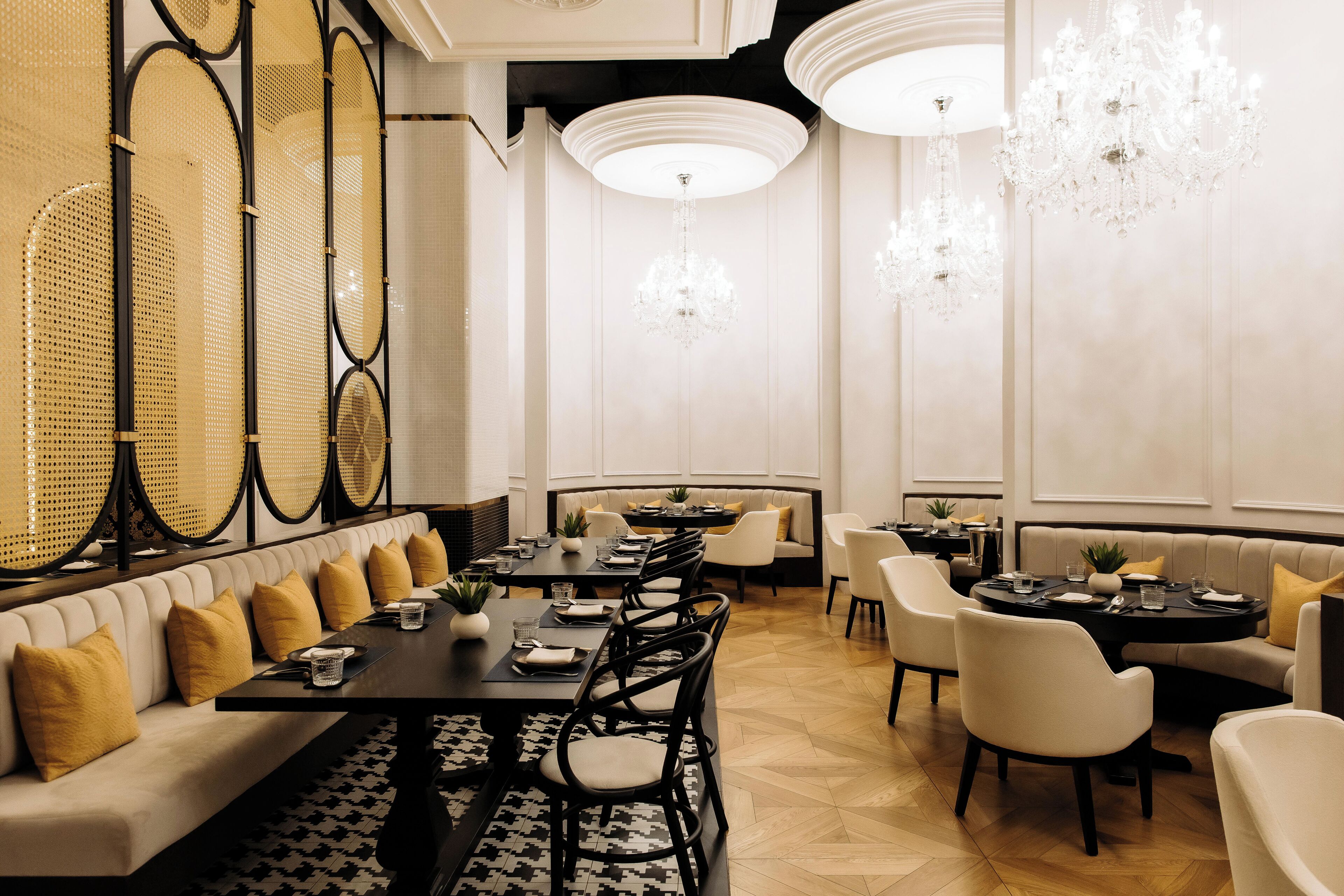 A modern dining area with a long table, cushioned seating, and decorative chandeliers.