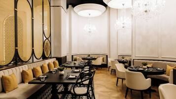 A modern dining area with a long table, cushioned seating, and decorative chandeliers.