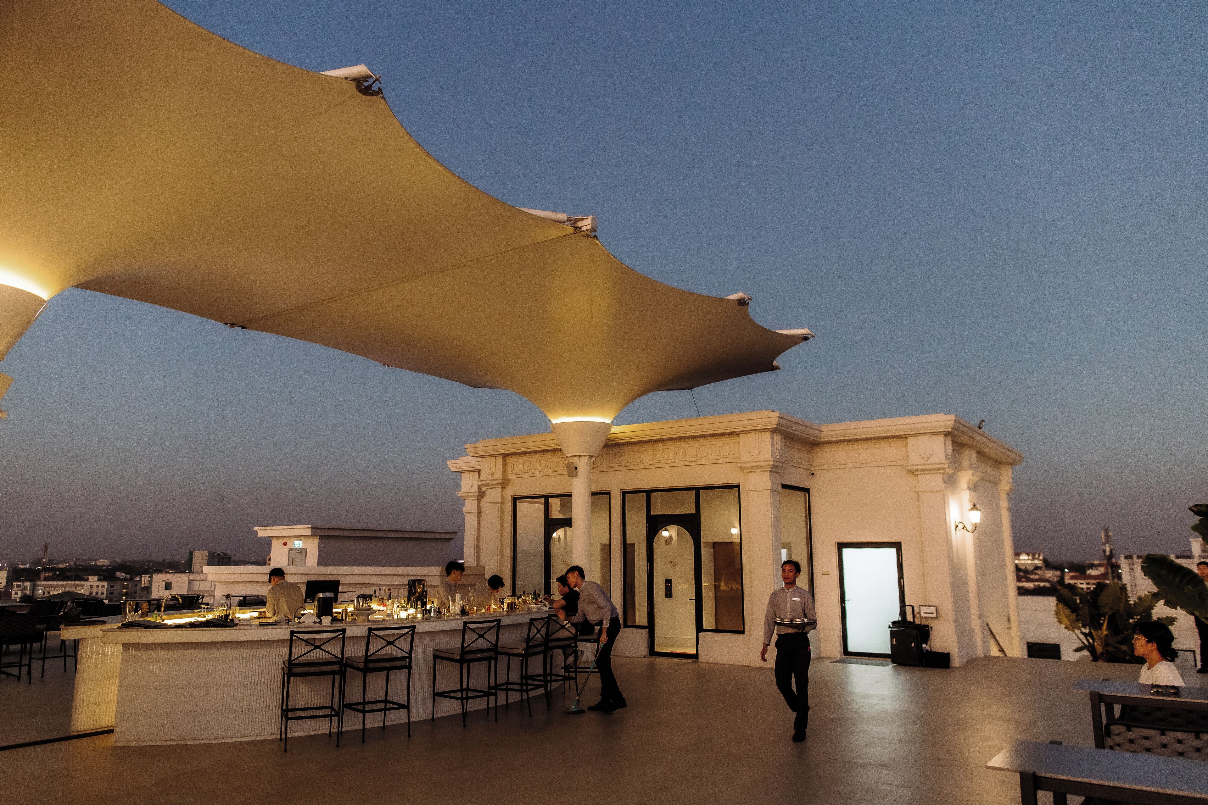 An outdoor bar area with a large canopy, bar stools, and a waiter.