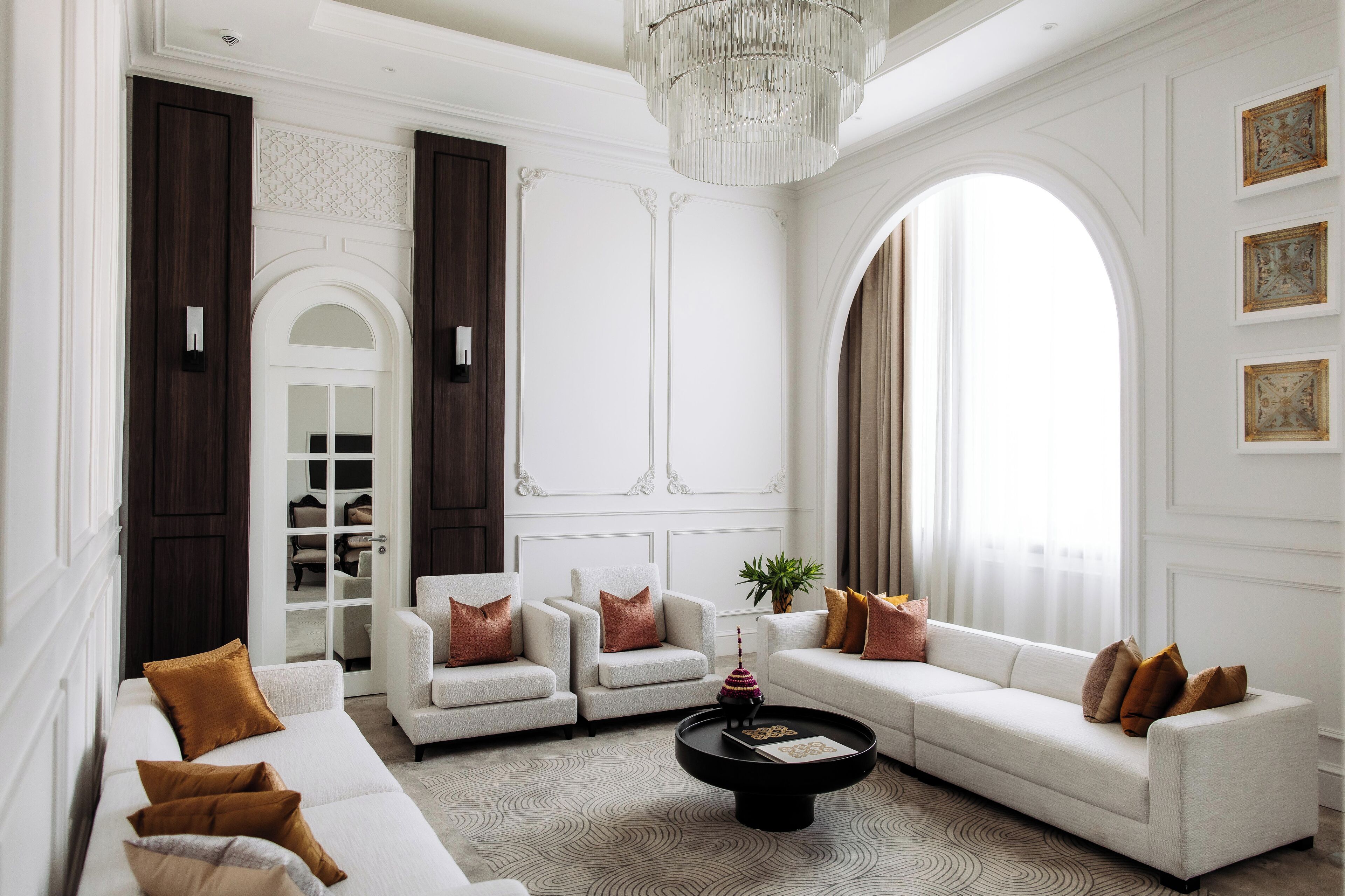 A spacious living room with a large arched window, a chandelier, and a white sofa set.