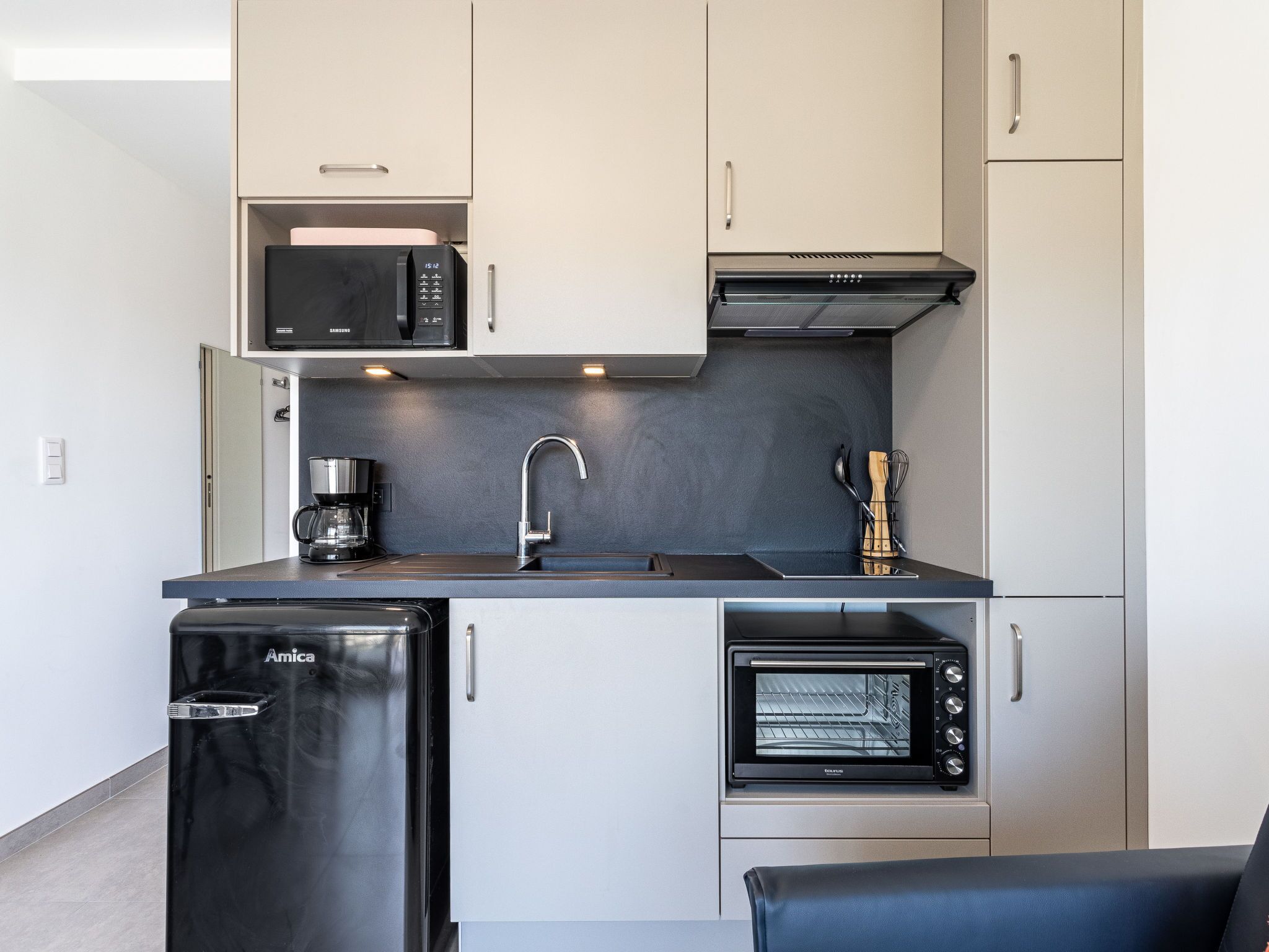 A compact kitchen with a microwave, toaster oven, sink, and a refrigerator.