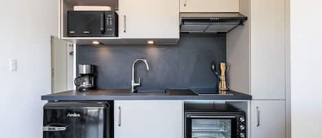 A compact kitchen with a microwave, toaster oven, sink, and a refrigerator.