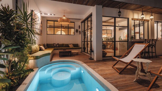 A modern outdoor pool area with a wooden deck, lounge chairs, and a seating area with a sofa and coffee table. - Arcadia Lodge (Canggu)