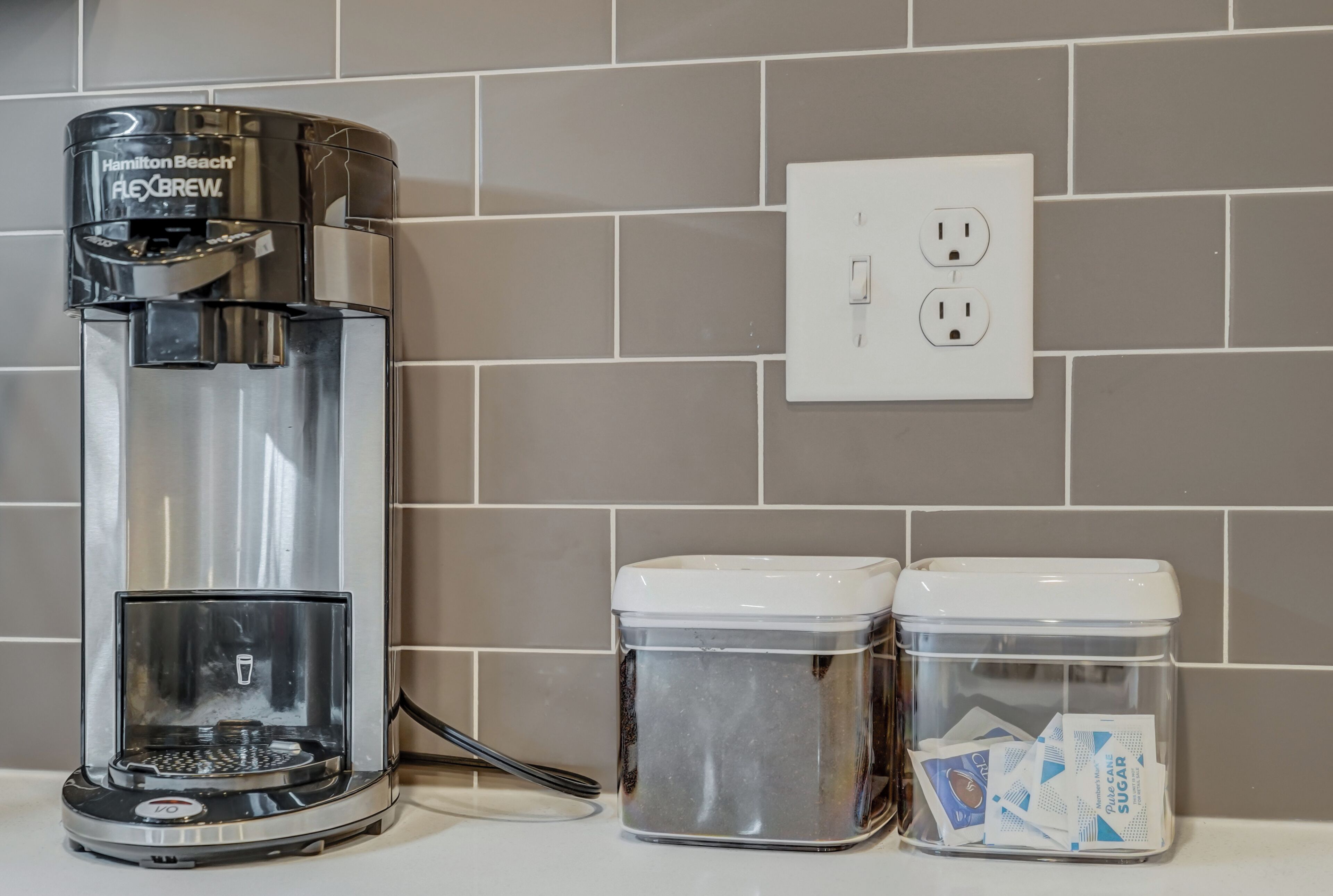 Eine Hamilton Beach Flexbrew Kaffeemaschine, zwei durchsichtige Behälter mit Deckeln und eine Steckdose.