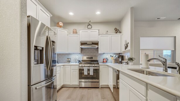 A modern kitchen with white cabinetry, stainless steel appliances, and a large island with a sink. - Sakura Springs (Colorado Springs)