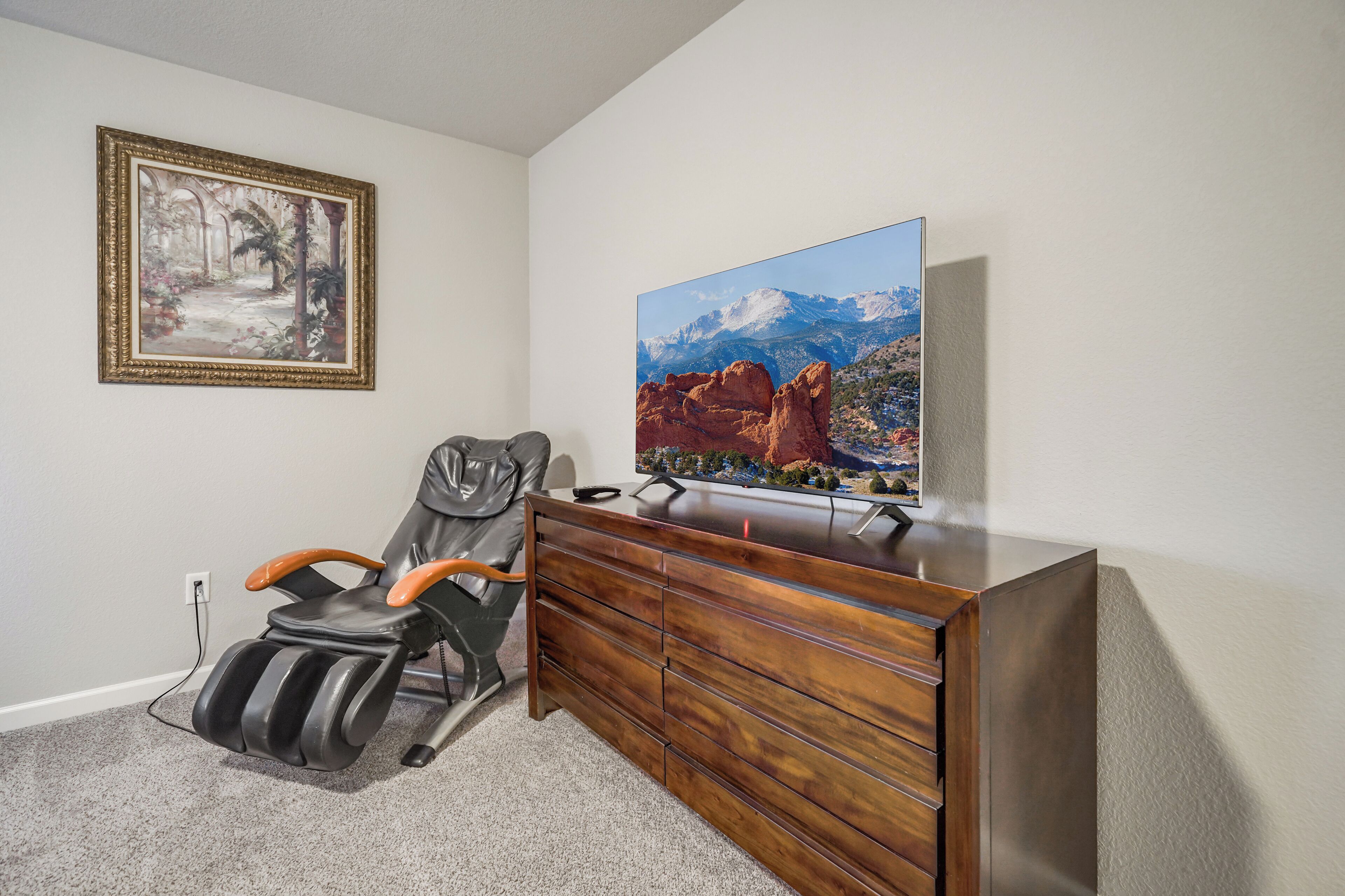 Ein Zimmer mit Massagegerät, einer Holzkommode, einem gerahmten Bild und einem großen Landschaftsbild an der Wand.