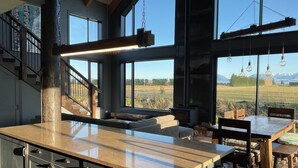 Una cocina moderna con una isla grande, un comedor con muebles de madera y vistas a un campo y montañas a través de amplios ventanales.