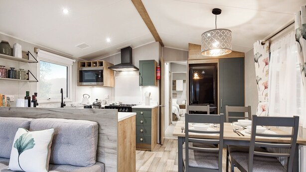 A compact kitchen with a dining area, a sofa with a decorative pillow, and a wooden ceiling. - Deluxe Plus Sierra 4 (Hunstanton)