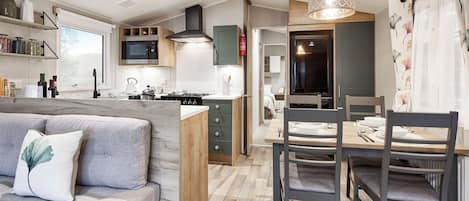 A compact kitchen with a dining area, a sofa with a decorative pillow, and a wooden ceiling.