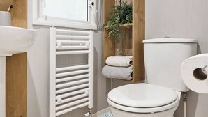A bathroom with a toilet, a white radiator, a wooden shelf with towels, and a window. - Deluxe Plus Sierra 4 (Hunstanton)