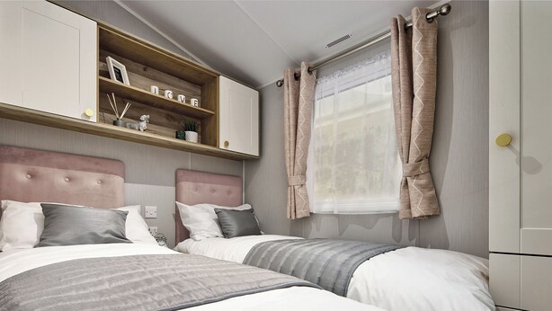 A bedroom with two beds, a wooden shelf with decorative items, a window with curtains, and a headboard. - Deluxe Plus Sierra 4 (Hunstanton)