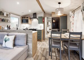 A compact kitchen with a dining area, a sofa with a decorative pillow, and a wooden ceiling.