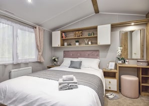 A bedroom with a bed, bedside tables, a vanity with a mirror, and a shelf with books and decorative items.