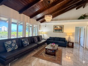 A spacious living room with a large window, a chandelier, a sofa, a coffee table, and a painting on the wall.