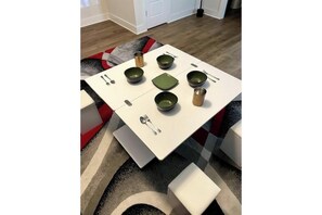 Une table à manger avec des bols, des cuillères et une assiette verte, le tout posé sur une nappe blanche.
