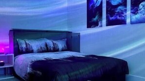 Une chambre à coucher comprenant un lit, une table de chevet et trois tableaux accrochés au mur.