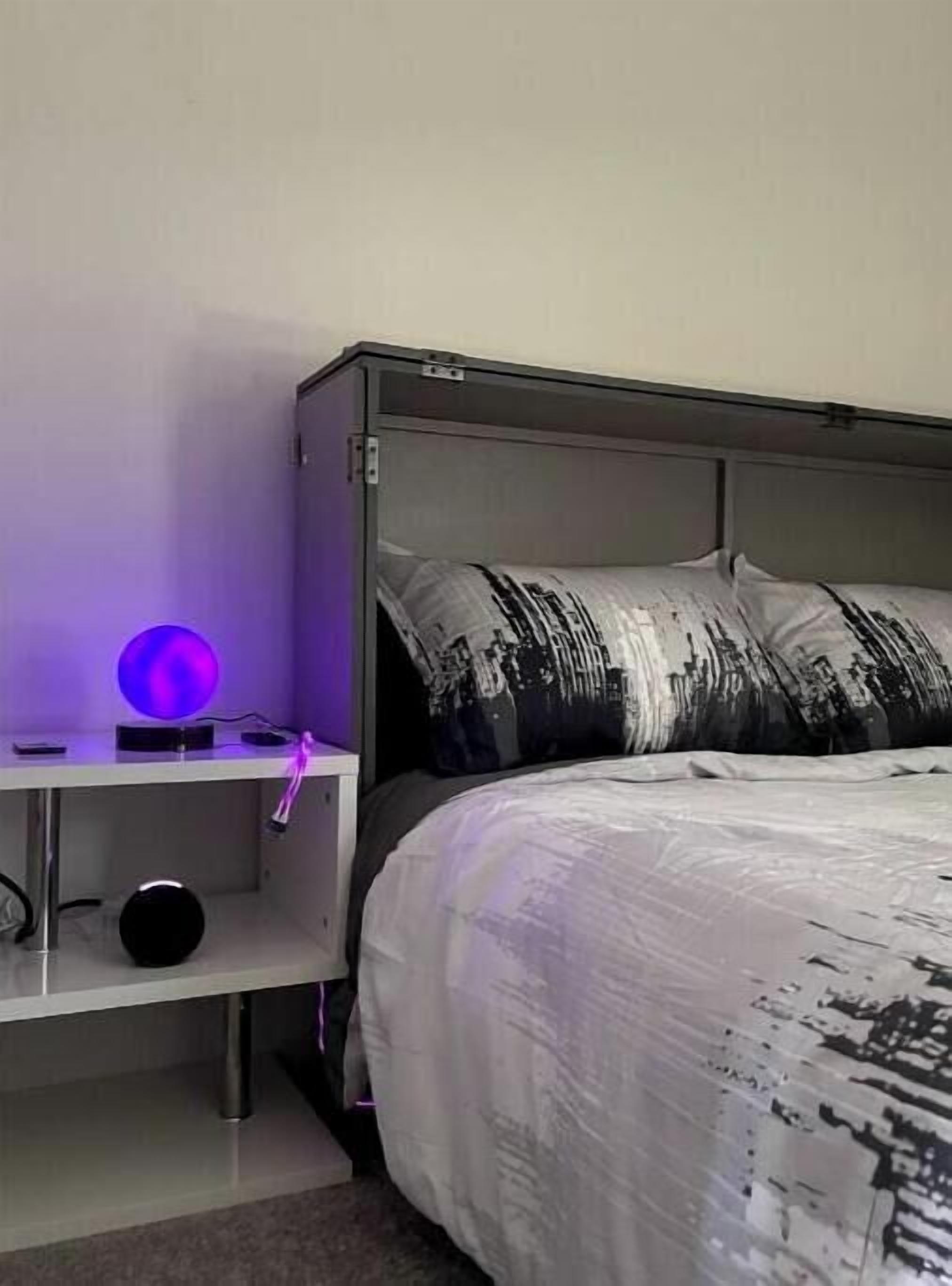 Een slaapkamer met een bed, een nachtkastje met een lamp en een wandplank.