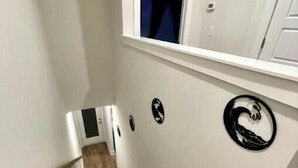 Un escalier étroit, avec des marches recouvertes de moquette et une rampe, menant à un palier doté d’une fenêtre et d’une porte.