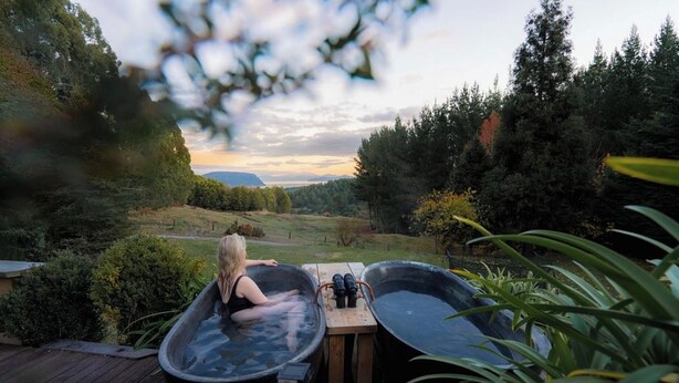 Iemand ontspant in een bubbelbad met een prachtig uitzicht op een bos en bergen op de achtergrond.
