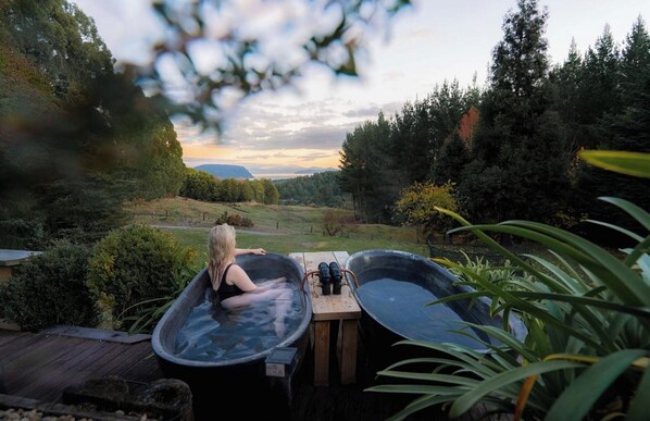 A person relaxing in a hot tub with a scenic view of a forest and mountains in the background.