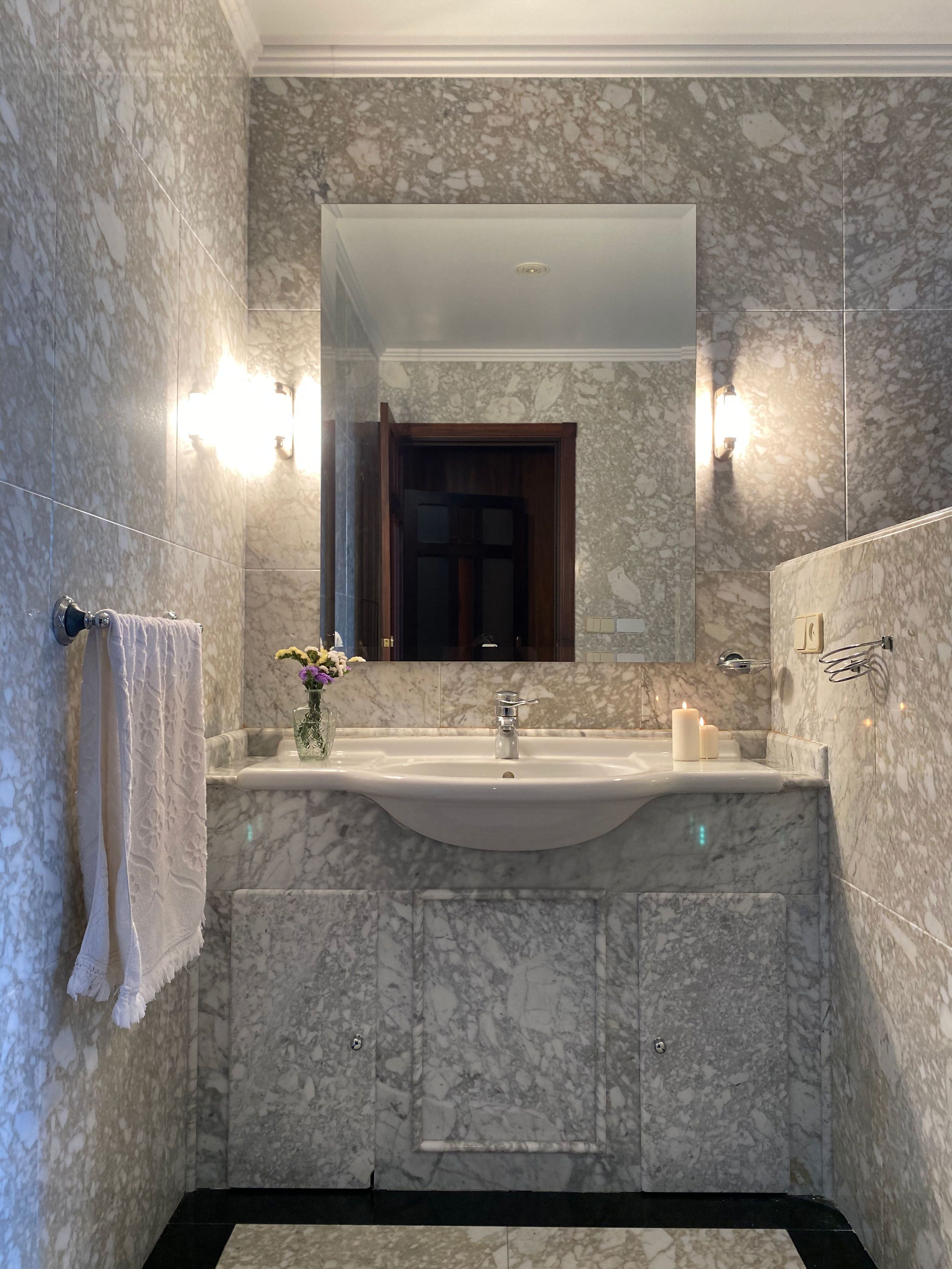 A bathroom with a marble sink, a mirror above it, and a towel hanging on the wall.