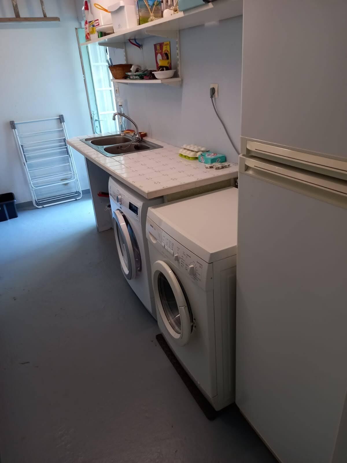 Un espace buanderie comprenant un lave-linge, un évier et un étendoir.