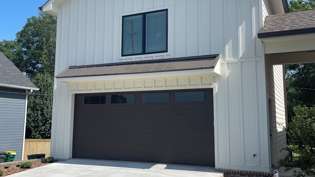 Een gelijkvloers huis met garage, een groot raam met luiken en een verzorgd gazon.