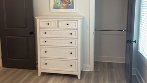 Een kamer met een houten vloer, een witte ladekast, een deur en een schilderij aan de muur.