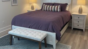 Een slaapkamer met een bed, nachtkastjes, een bankje en een plafondventilator.