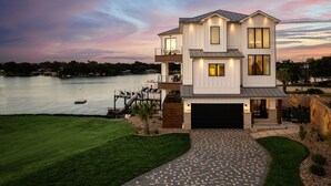 Ein zweistöckiges Haus mit Garage, einem Steg und Blick auf einen See im Dämmerlicht.