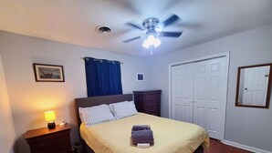 A bedroom with a bed, a nightstand, a dresser, a ceiling fan, and a door.