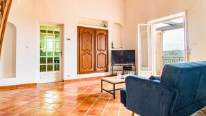 Ein geräumiges Wohnzimmer mit großem Fernseher, einem blauen Sofa und Fliesenboden.