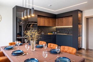 Een moderne keuken met donkere kastjes, een marmeren spatwand en een eethoek met een tafel gedekt voor zes personen.