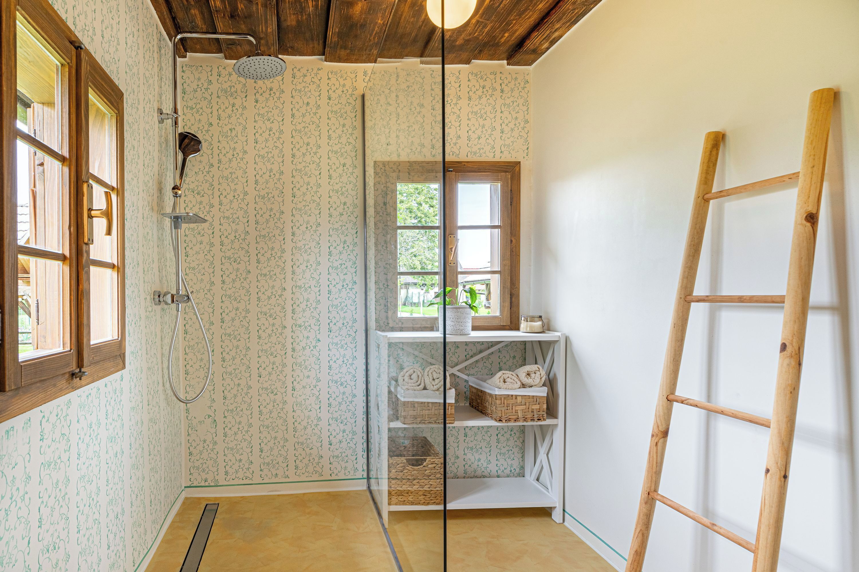 Een badkamer met een douche, een houten trap en een raam met uitzicht op groen.