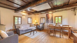 A cozy living room with a wooden ceiling, a grey sofa, a dining table with chairs, and a small side table with a lamp. - Mimi Cottage w/ Sauna near Kolpa River, Gradac, Slovenia (Gradac)
