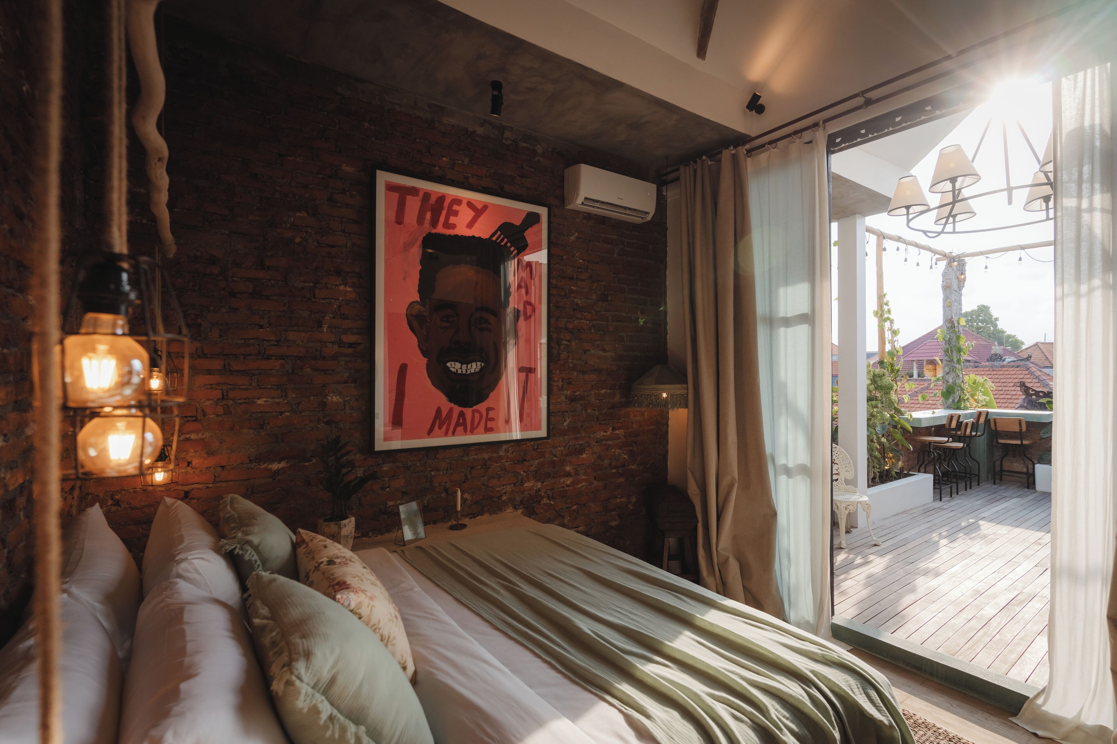 Ein Schlafzimmer mit Backsteinwand, einem Bett mit Kissen, einem Poster und Blick auf eine Terrasse.