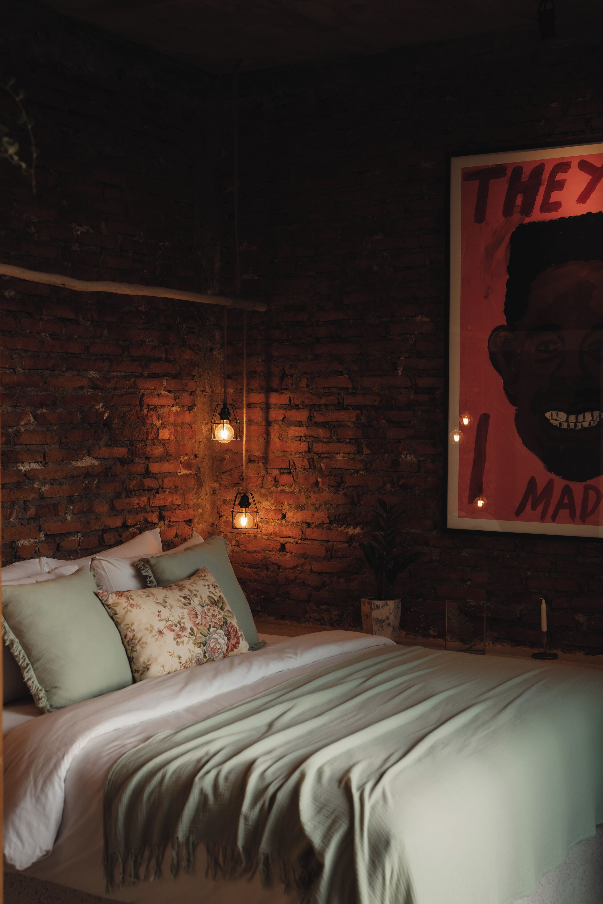 Un dormitorio con pared de ladrillo, una cama con almohadas y un cartel en la pared.