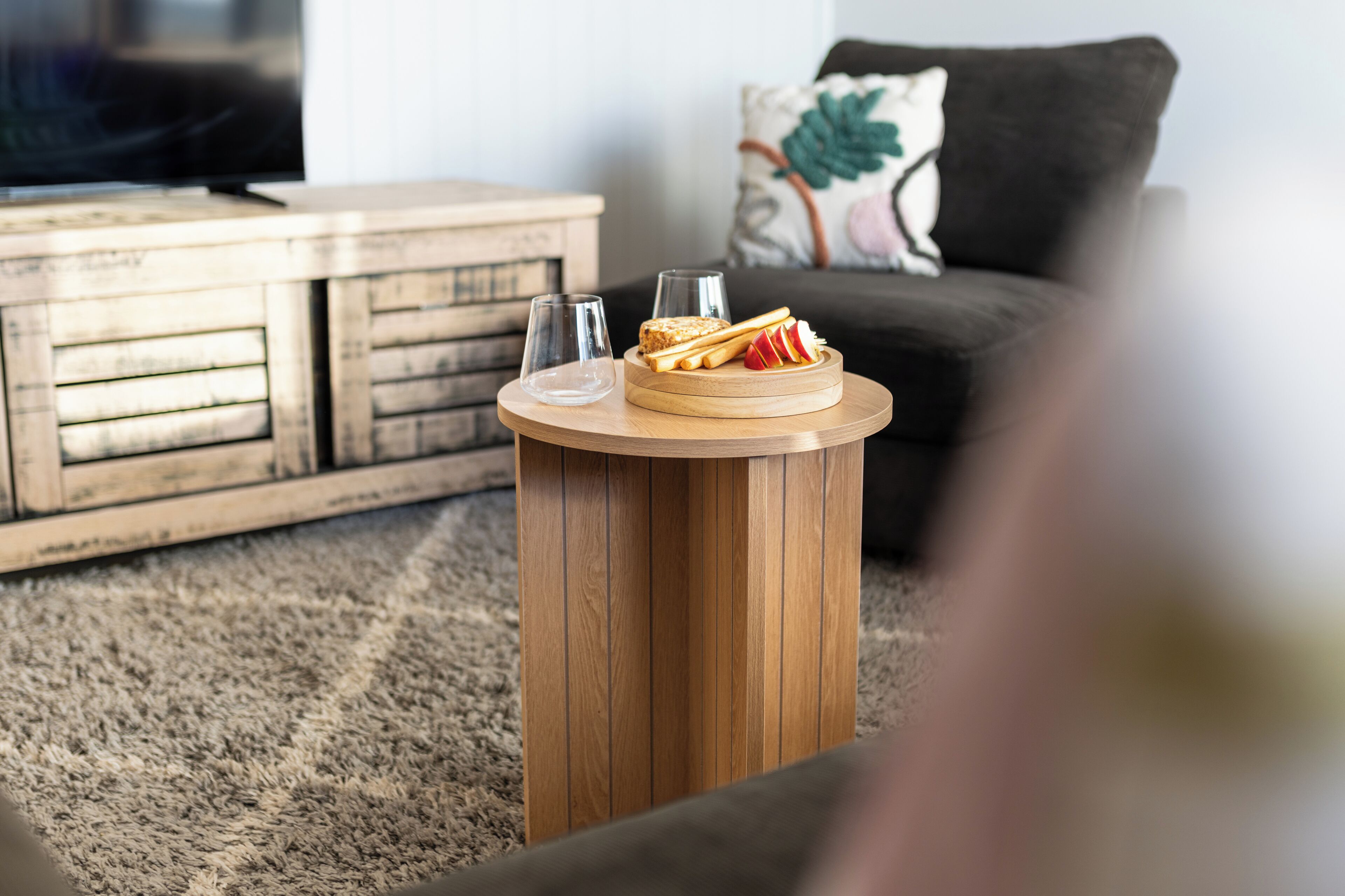 A wooden coffee table with two glasses and a plate of food in a living room.
