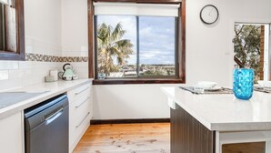 Een moderne keuken met een vaatwasser, een raam met uitzicht op palmbomen en een klok aan de muur.