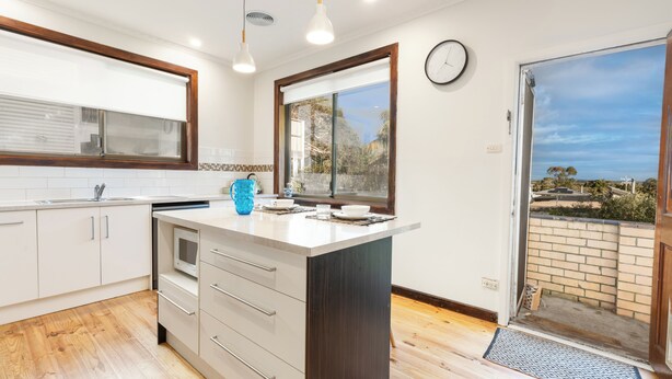 Een moderne keuken met witte kasten, een donker eiland en een groot raam met uitzicht op de omgeving.