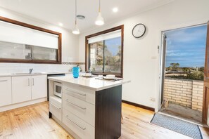 A modern kitchen with white cabinets, a dark island, and a large window offering a view of the outdoors. - Pet friendly Oasis w/ Enchanting Sunset View (Ocean Grove)
