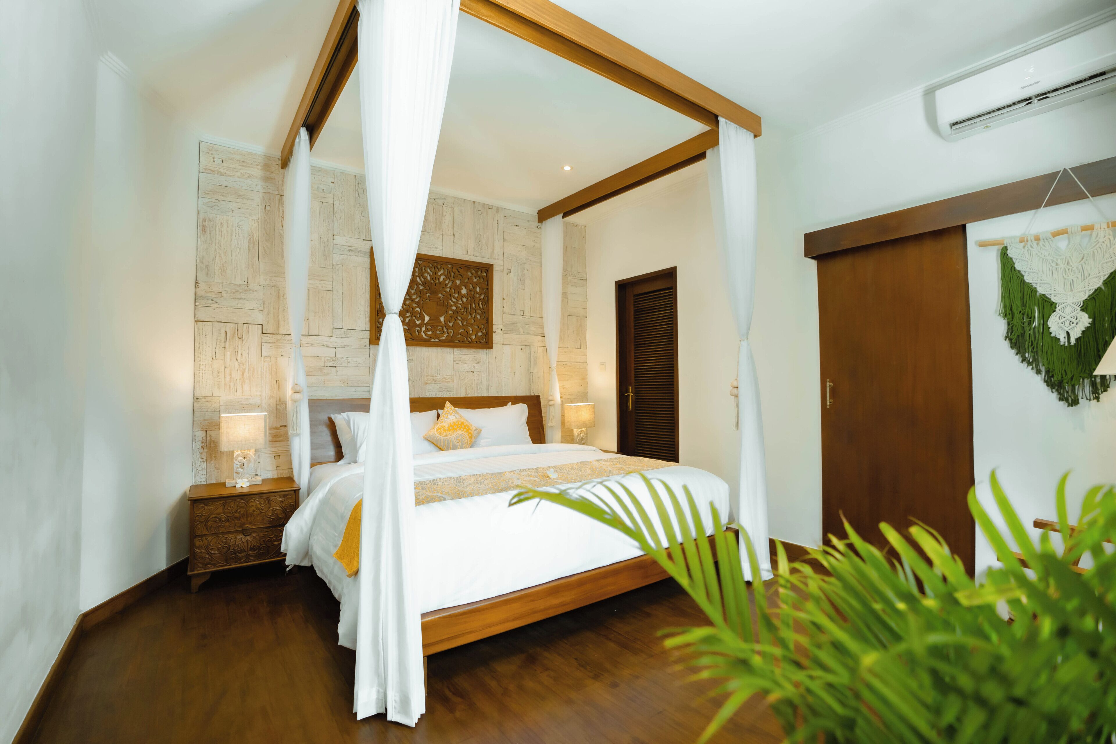Camera da letto con letto a baldacchino, pavimento in legno, comodino con lampada e climatizzatore a parete.
