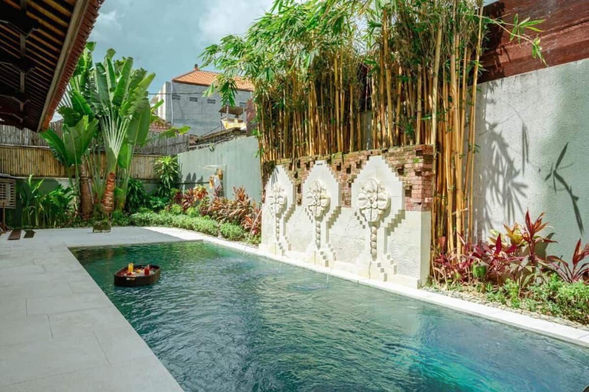 Une piscine agrémentée d’un mur décoratif, entourée d’une végétation luxuriante et d’une structure en bambou.