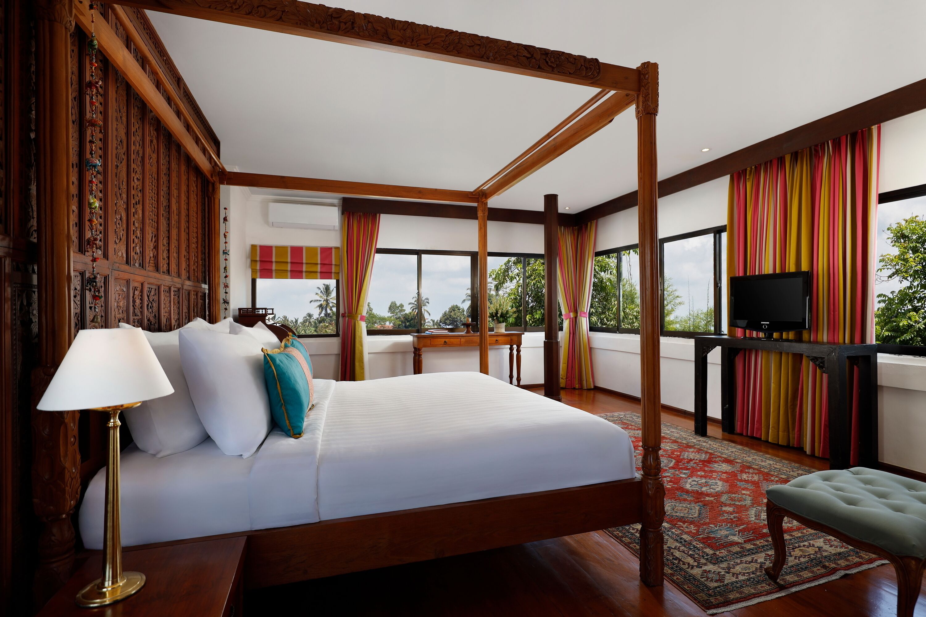 Una cama con dosel con un edredón blanco, una lámpara dorada y una almohada color turquesa.