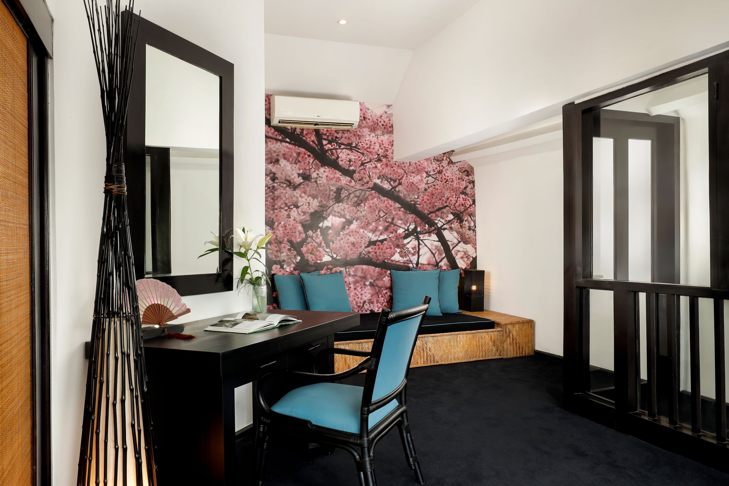 A modern room with a dining area, a sofa with teal cushions, a black chair, and a large wall mural of cherry blossoms.