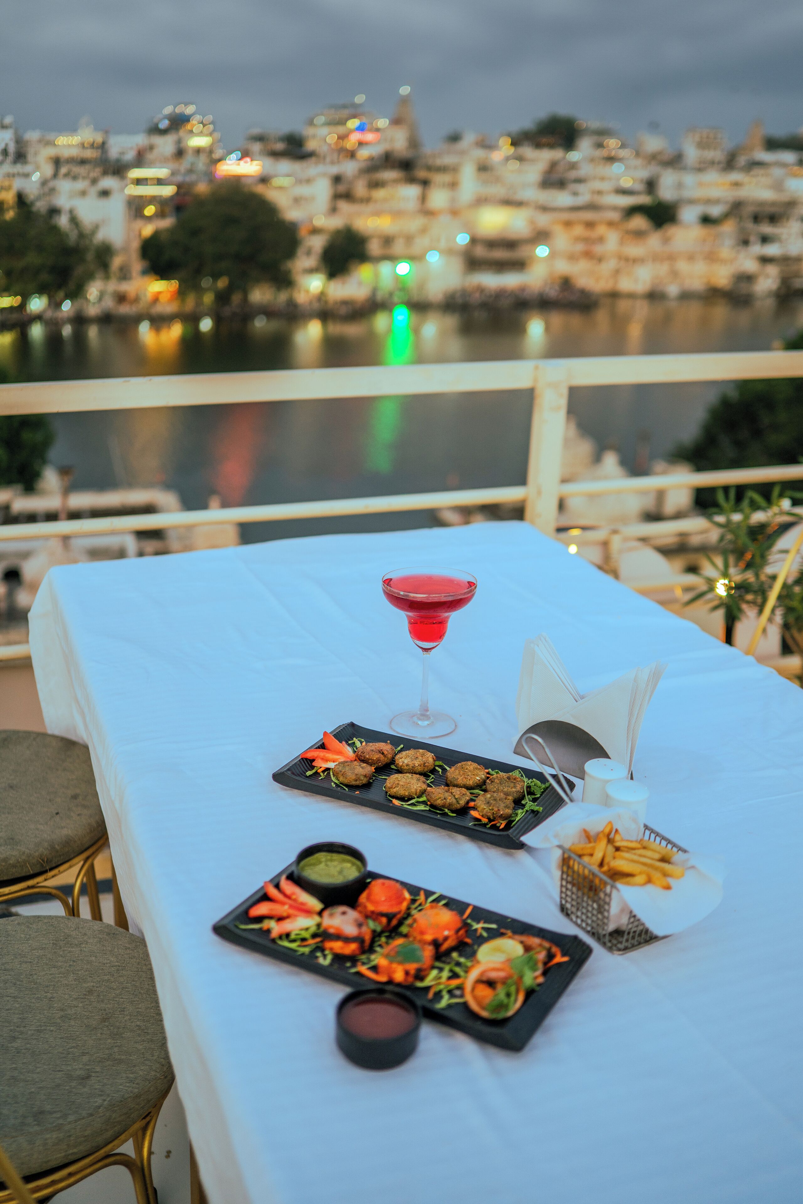 A table set with food and drinks on a balcony overlooking a cityscape.