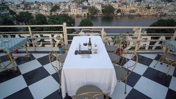 Une table dressée avec une bouteille, des verres et des amuse-gueules sur une terrasse dont le sol est à carreaux et qui est équipée de chaises en métal.