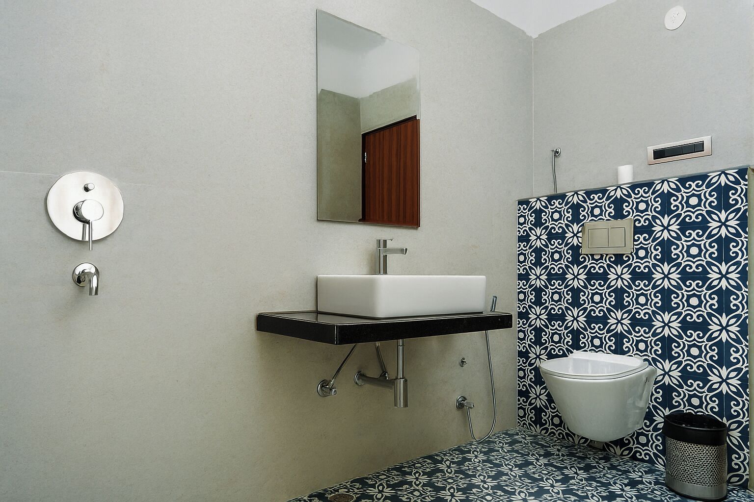 A bathroom with a white sink, a mirror, a toilet, and patterned tiles.